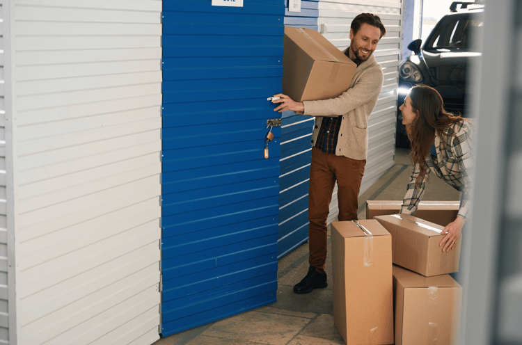 Young man and woman with big cardboard boxes in self storage unit