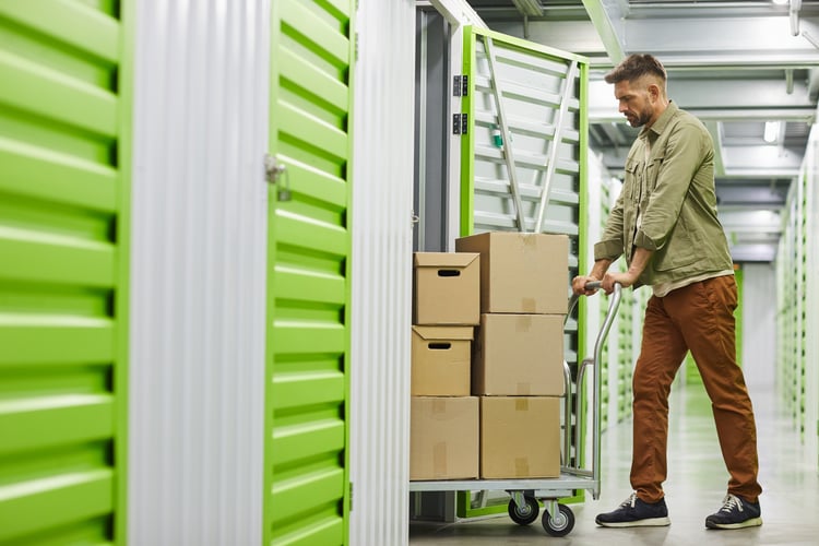 man loading cart with cardboard boxes into self storage unit